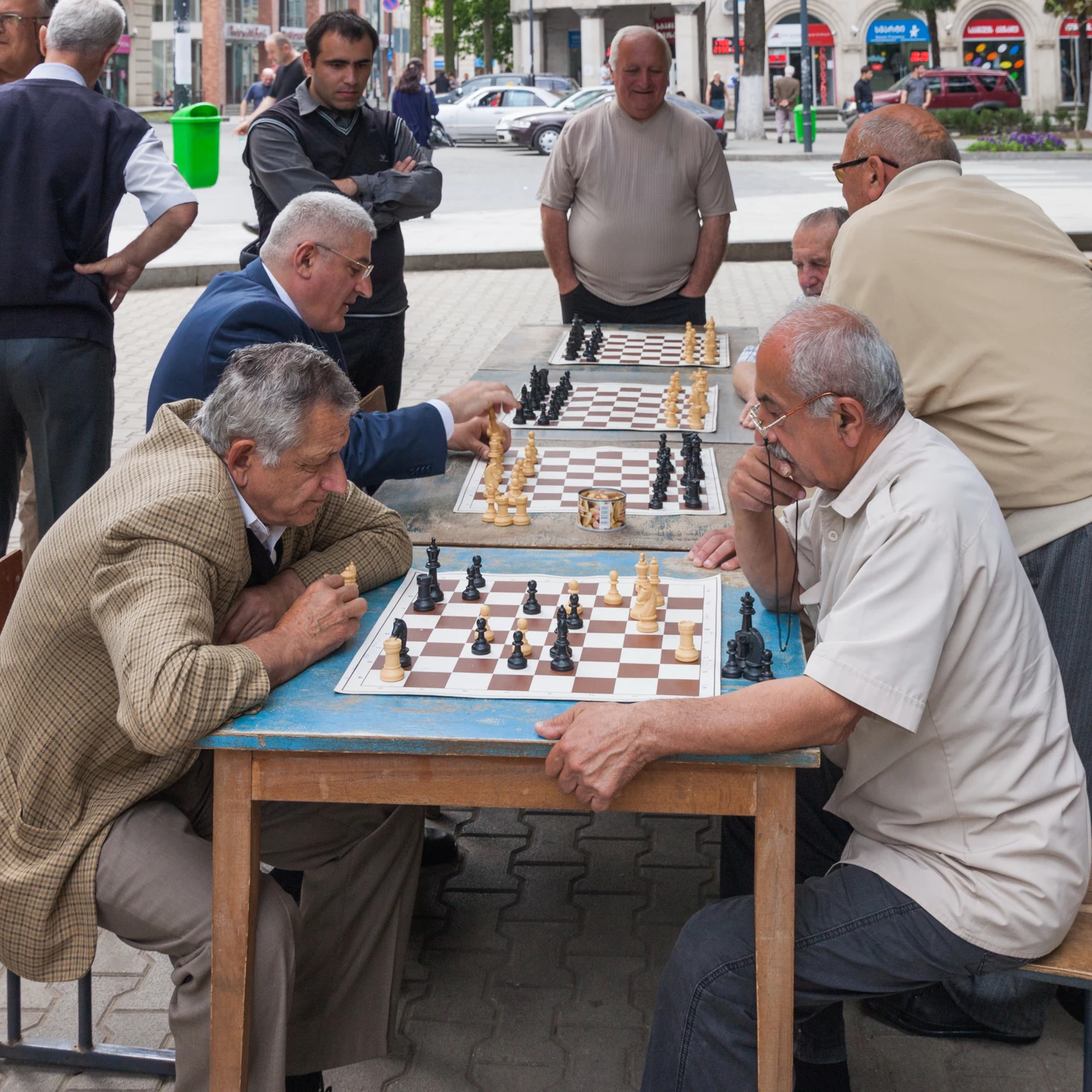 多位老人围坐在街边木桌旁下棋