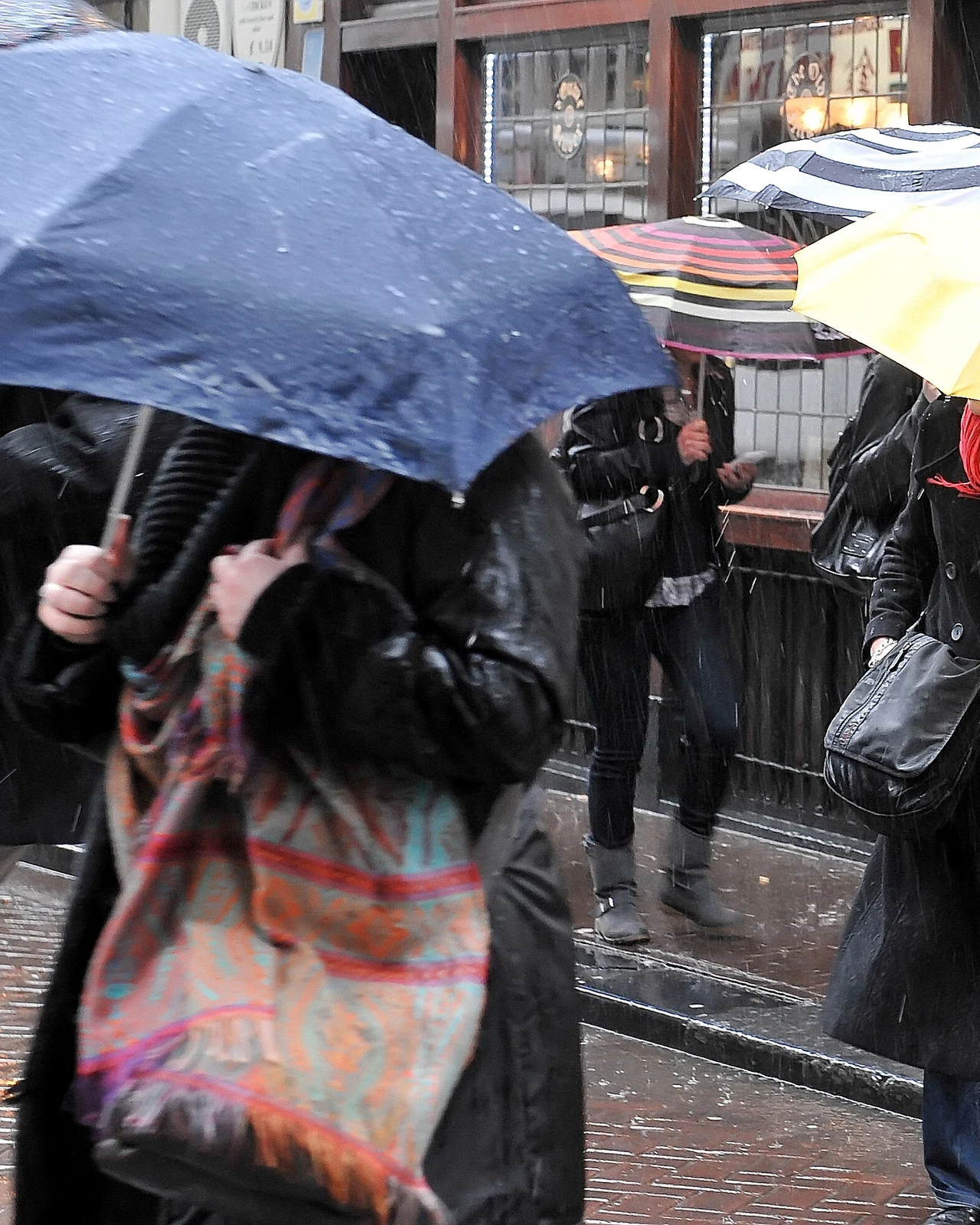 雨中城市街道上撑着深蓝、黄色与条纹雨伞的行人